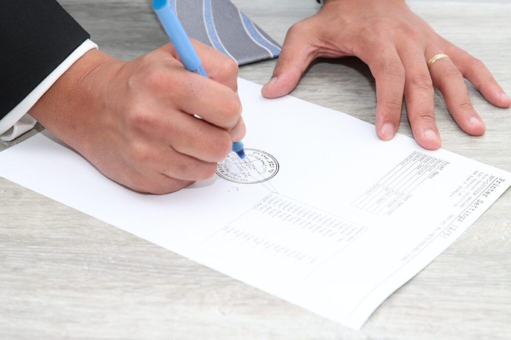 Hand in a suit sleeve signing a paper document on a desk