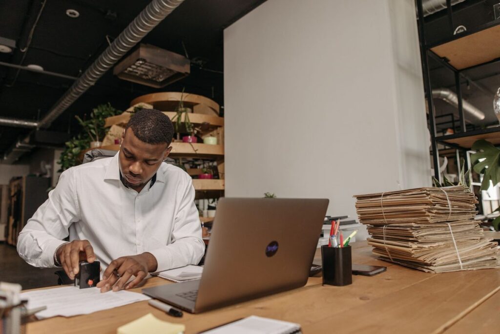 Man stamping documents at an office desk with a laptop, preparing a certified true copy in Fujairah